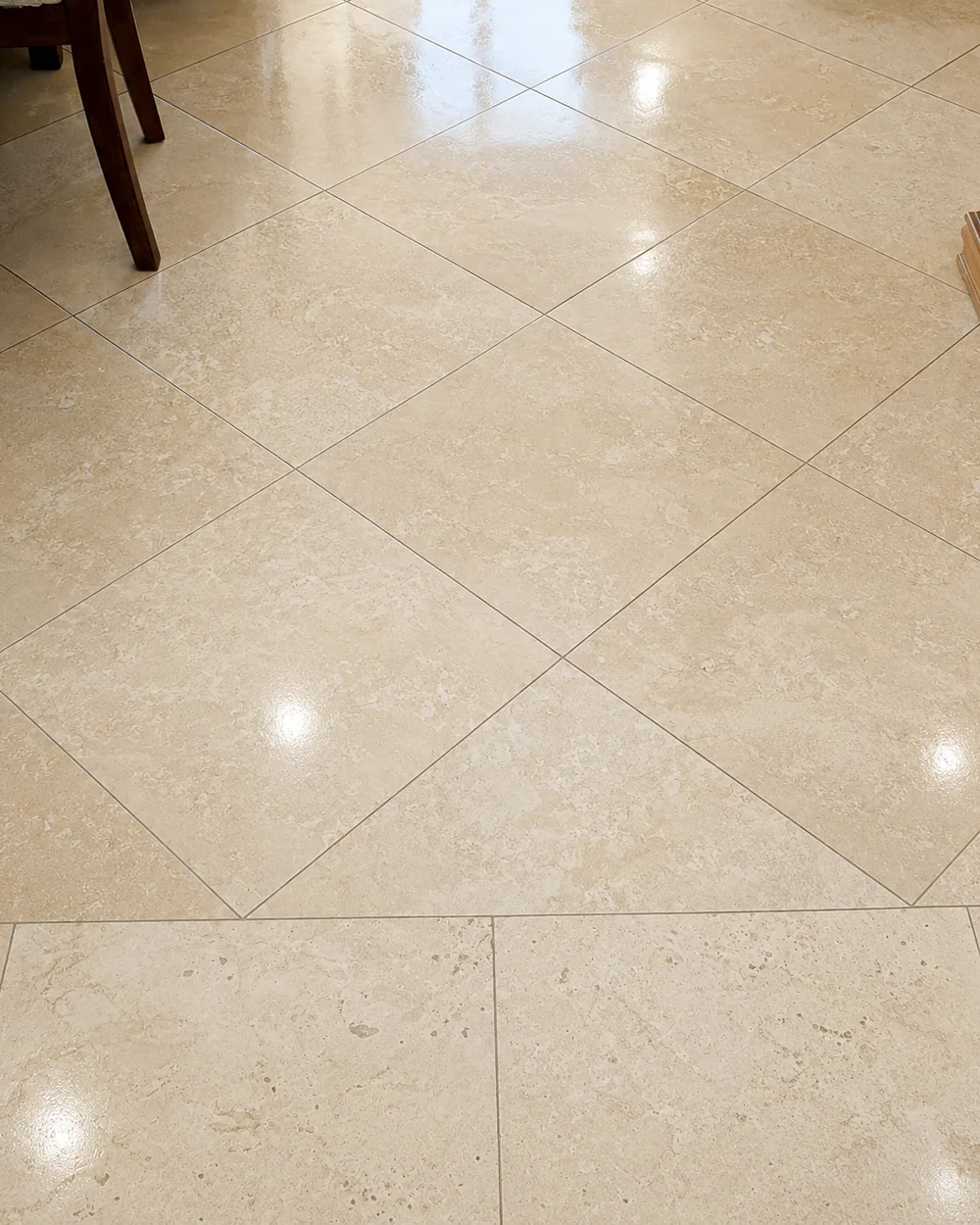 Travertine floor tile polished to an even sheen, the ceiling light reflected across the joints