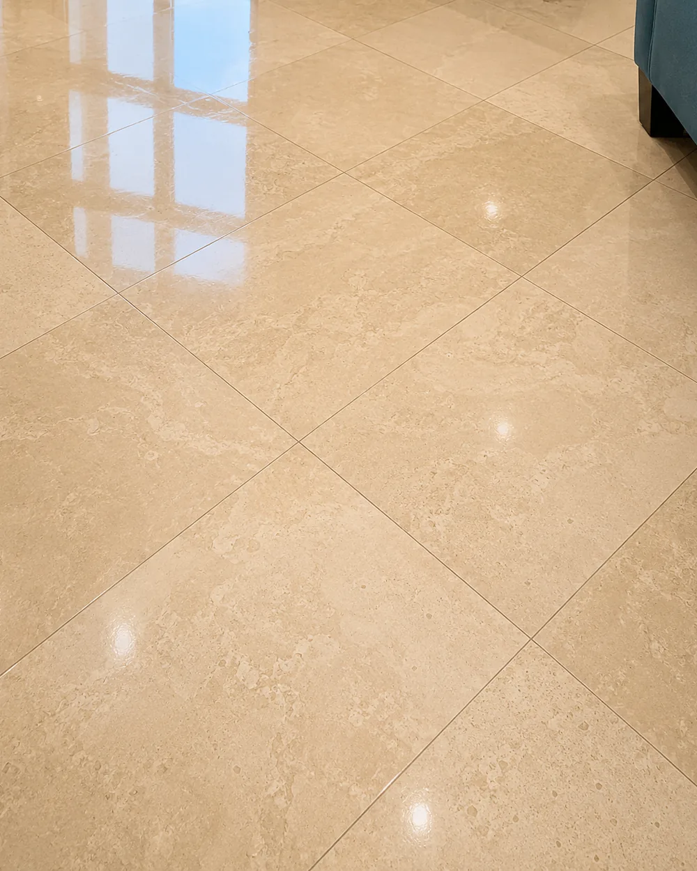 Close view of travertine tile refined to a high polish, ceiling lights mirrored in the surface